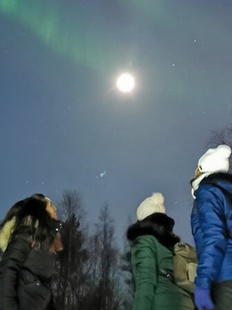 Friends watching northern lights in Lapland under a moonlit sky.