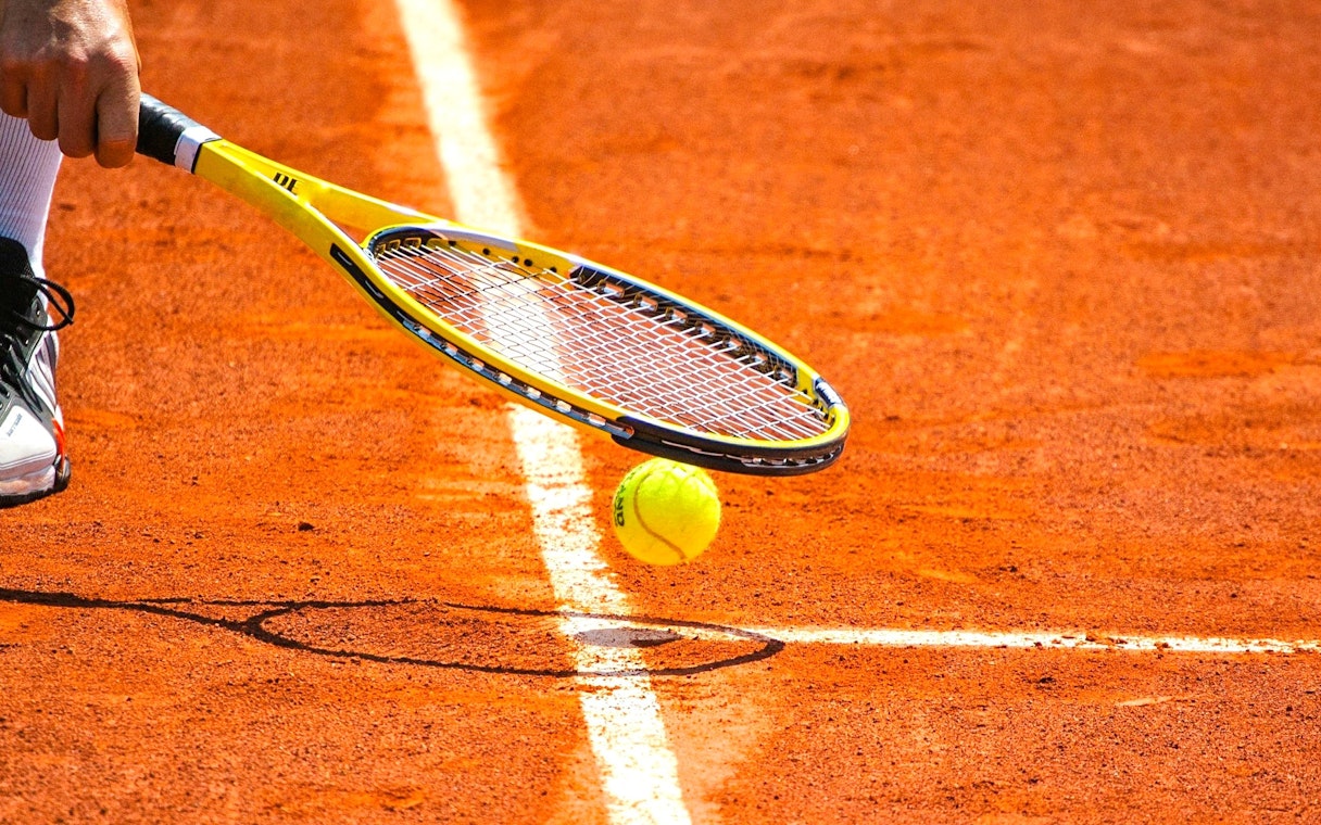 Tennis ball and racket on clay court at Roland-Garros Stadium.