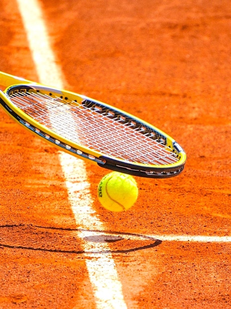 Tennis ball and racket on clay court at Roland-Garros Stadium.