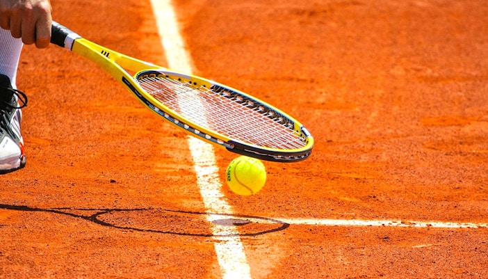 Tennis ball and racket on clay court at Roland-Garros Stadium.