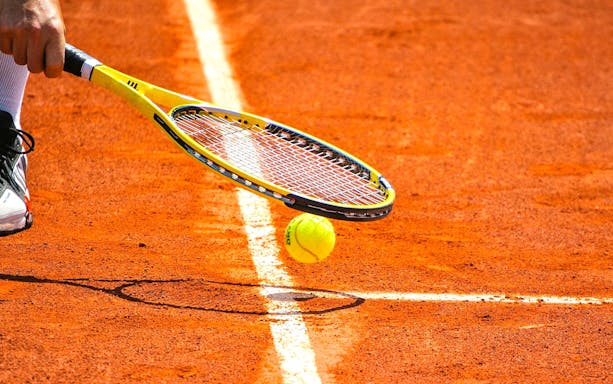 Tennis ball and racket on clay court at Roland-Garros Stadium.