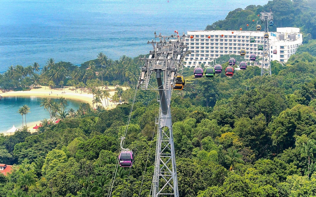 Singapore Cable Car over lush greenery and beach, with ocean view in the background.