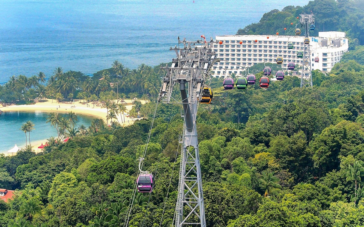 Singapore Cable Car over lush greenery and beach, with ocean view in the background.