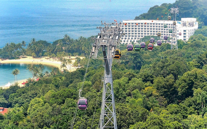 Singapore Cable Car over lush greenery and beach, with ocean view in the background.