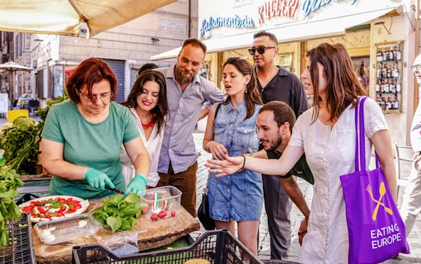 Tour group in Rome watching Signora Cristina prepare local food at a market.