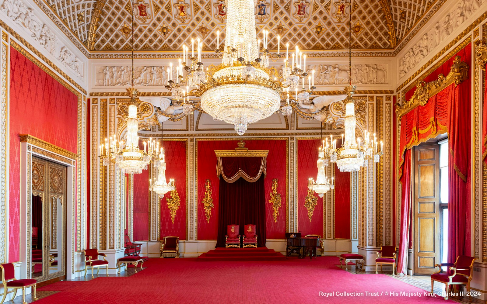 Throne Room at Buckingham Palace with ornate chandeliers and red decor.