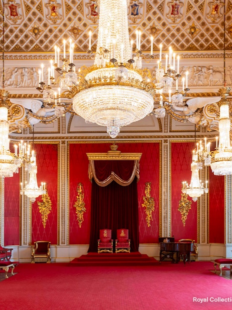 Throne Room at Buckingham Palace with ornate chandeliers and red decor.