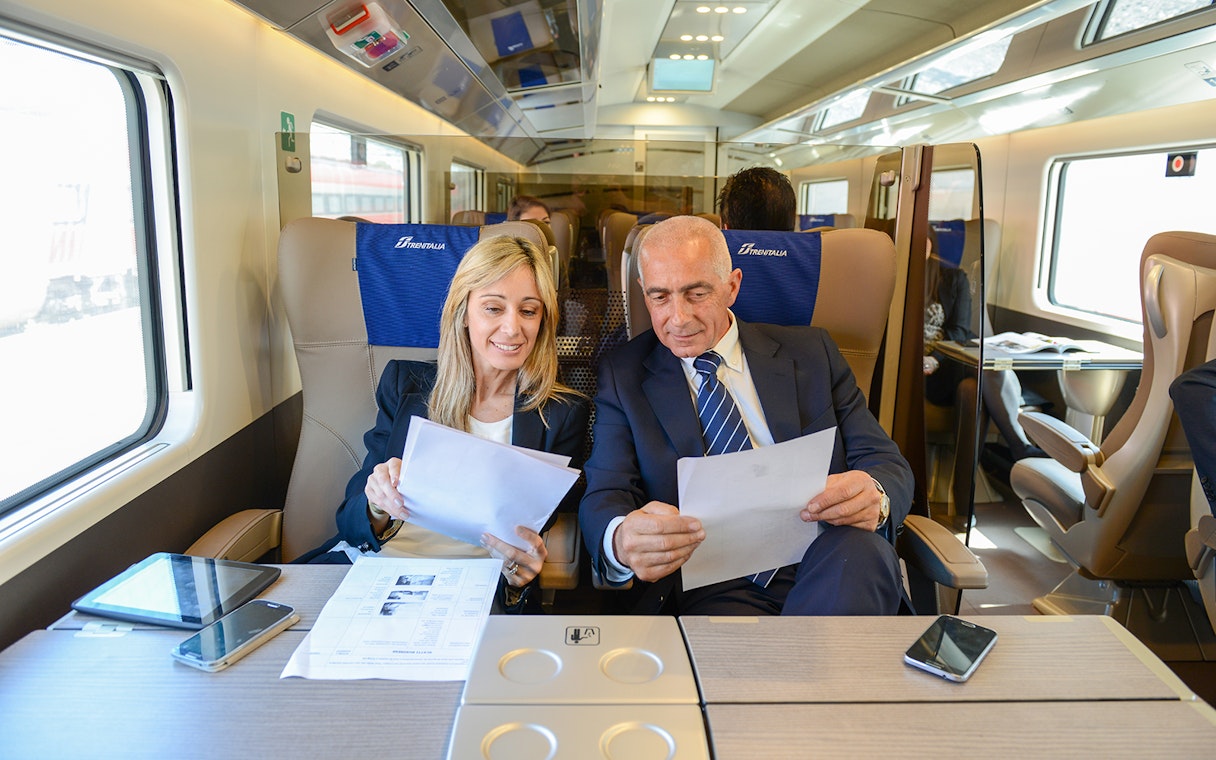 Passengers reviewing documents in first-class seats on a Trenitalia train with Eurail Global Pass.