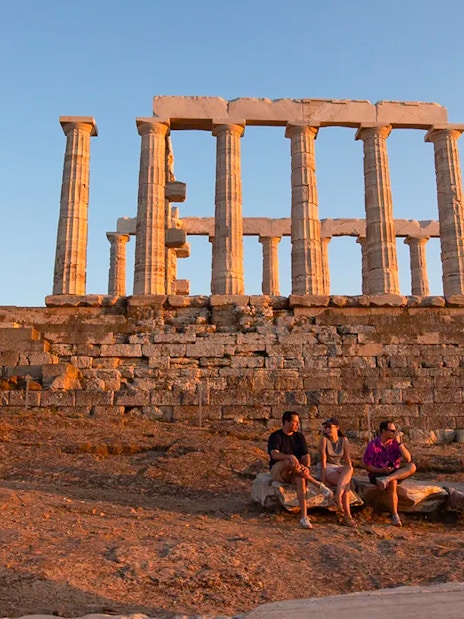 Temple of Poseidon at sunset with visitors seated on ancient stones.