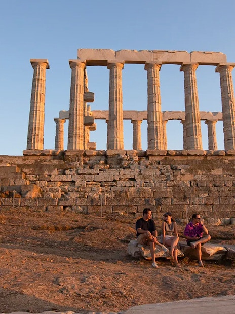 Temple of Poseidon at sunset with visitors seated on ancient stones.