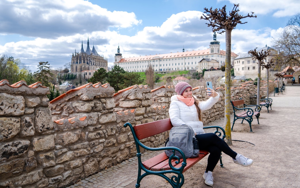 Tourist taking a selfie on a bench in Kutná Hora with the Cathedral of St. Barbara in the background.