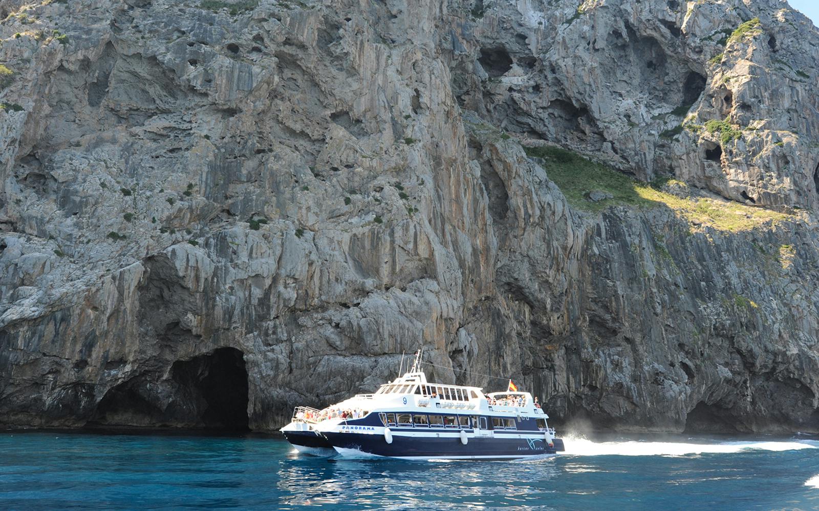 Boat cruising near rocky cliffs on Mallorca sightseeing tour.