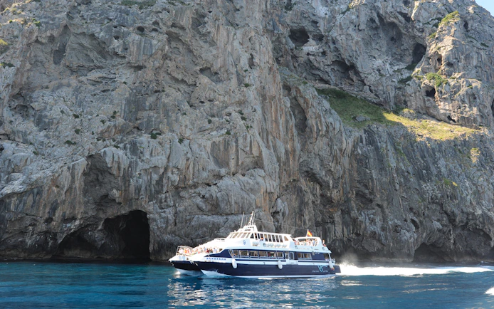 Boat cruising near rocky cliffs on Mallorca sightseeing tour.