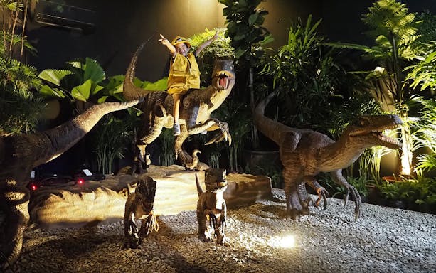 Child riding a dinosaur model at Dinoland Singapore exhibit.