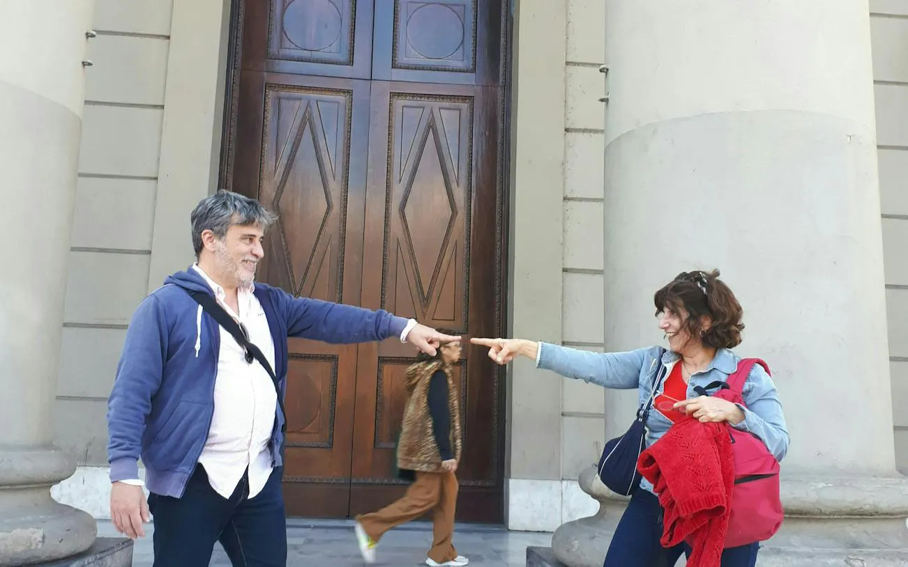 Two people pointing at each other in front of a historic building on Avenida de Mayo, Buenos Aires.