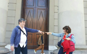 Two people pointing at each other in front of a historic building on Avenida de Mayo, Buenos Aires.