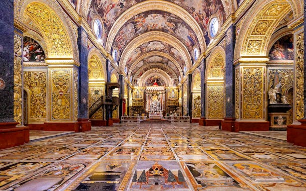 Interior of St. John's Co-Cathedral in Valletta, featuring ornate gold decorations and detailed frescoes.