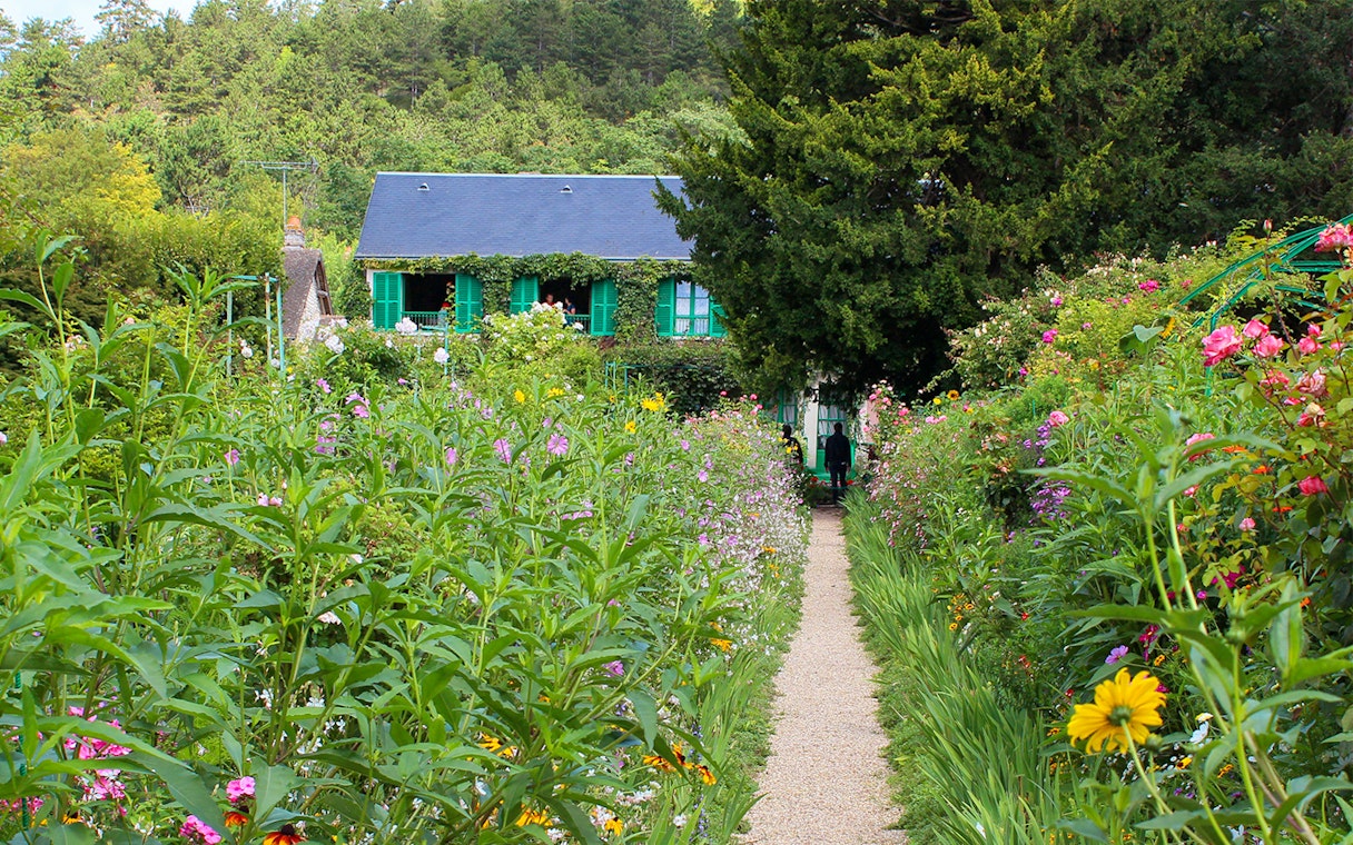 Pathway through Monet's garden leading to his house in Giverny, surrounded by vibrant flowers.