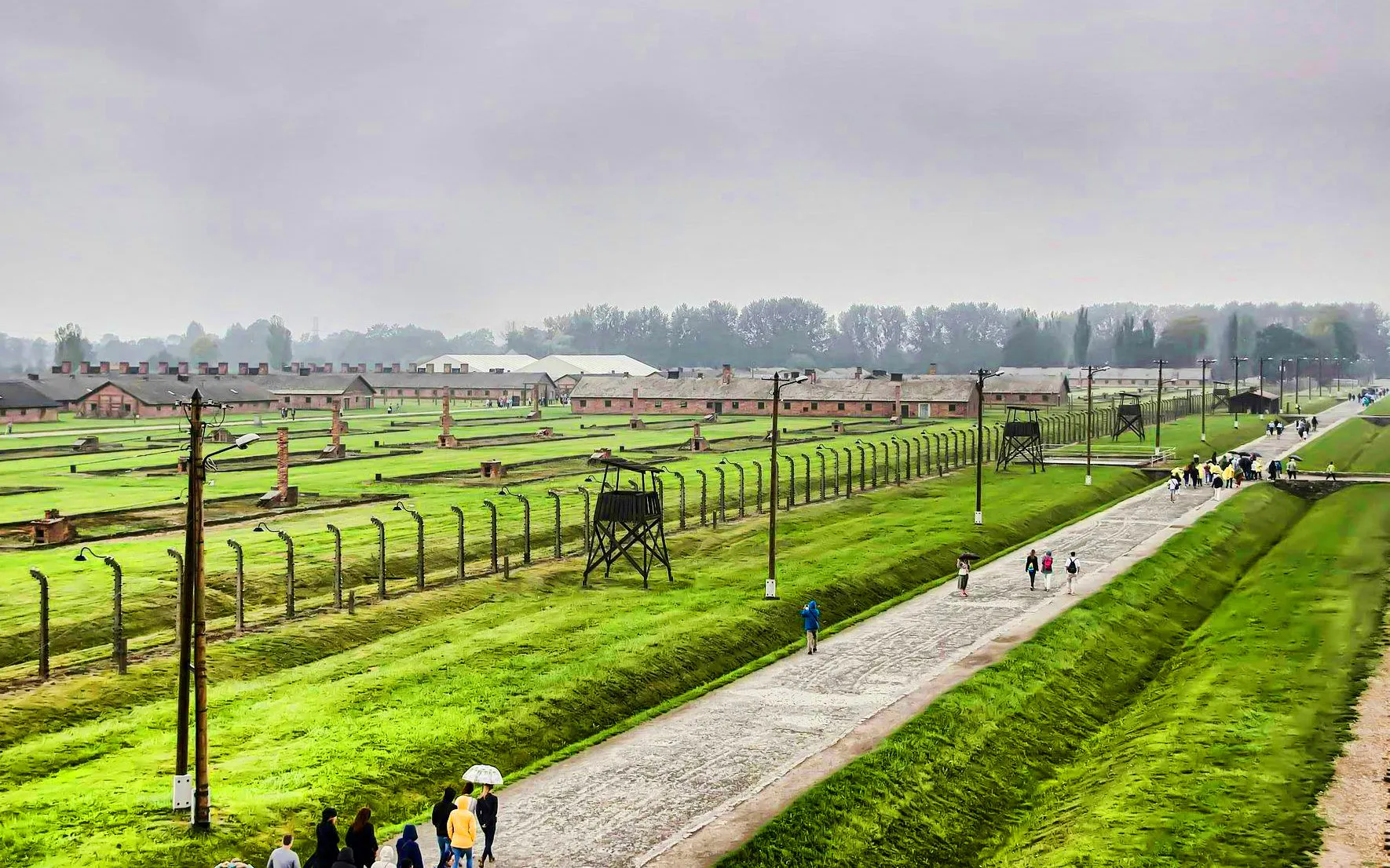 Auschwitz Birkenau II watchtower overlooking barracks and visitors walking along the path.