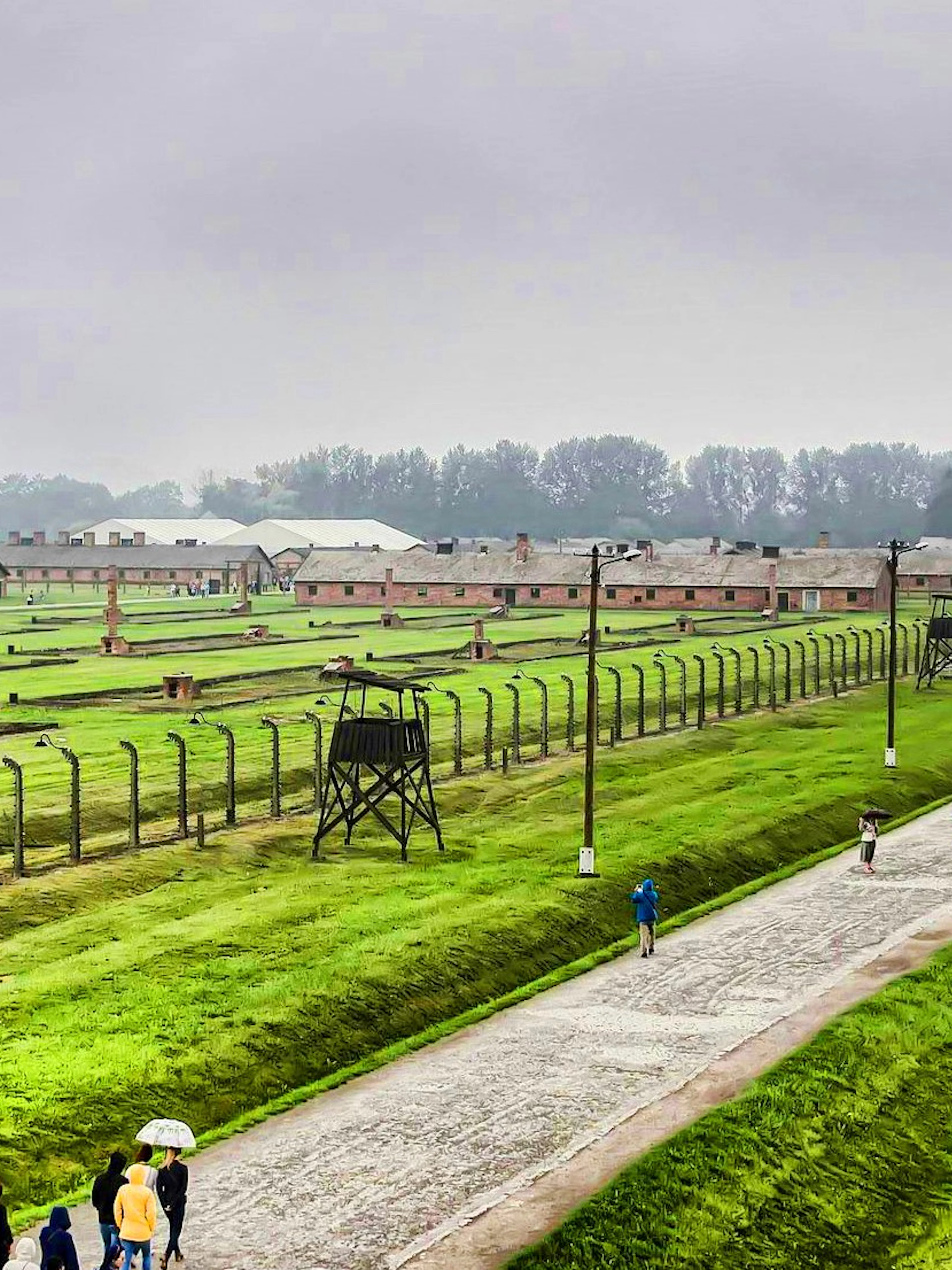 Auschwitz Birkenau II watchtower overlooking barracks and visitors walking along the path.