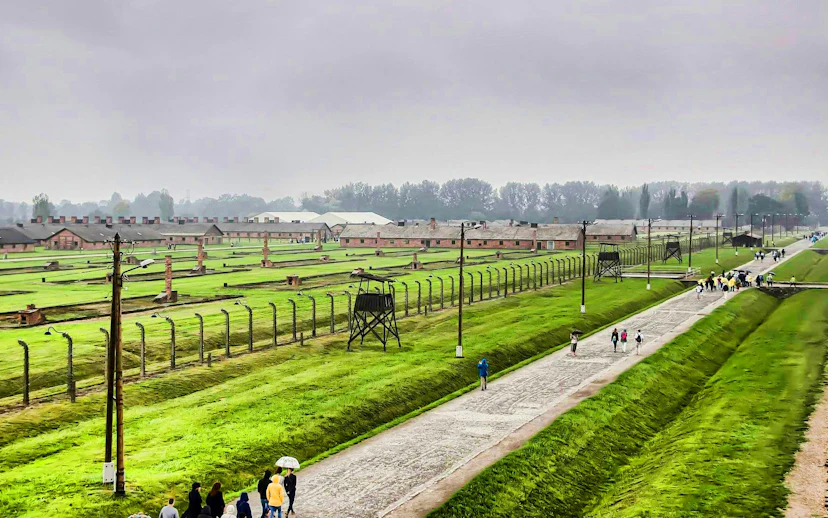 Auschwitz Birkenau II watchtower overlooking barracks and visitors walking along the path.