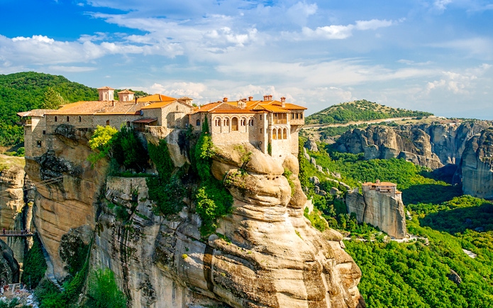 Meteora monastery perched on a rock formation in Greece, surrounded by lush green landscape.