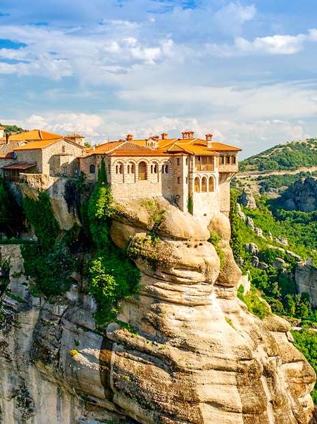 Meteora monastery perched on a rock formation in Greece, surrounded by lush green landscape.