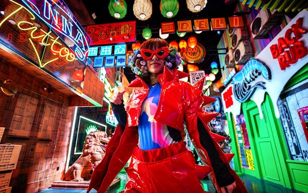 Colorful character in vibrant outfit at House Of Hype surrounded by neon signs.