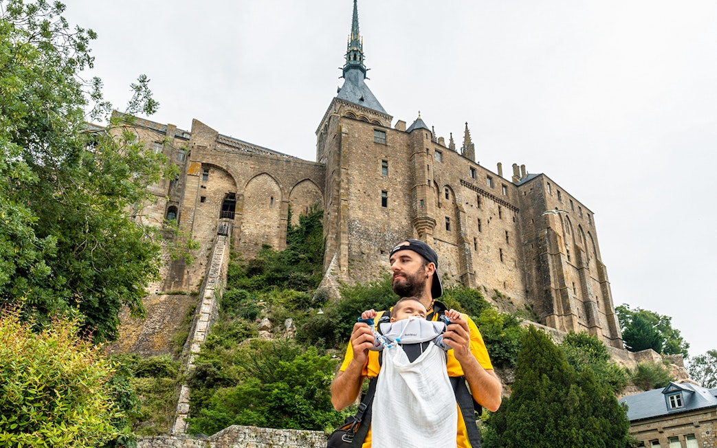 Father with baby in carrier visiting Mont Saint Michel Abbey, France.