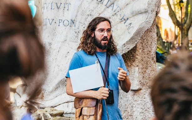 Tour guide explaining historical artifacts inside Roman catacombs, Italy.