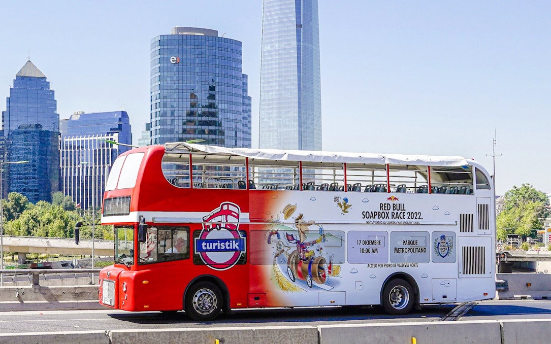 Red double-decker bus on Santiago city tour with skyscrapers in the background.