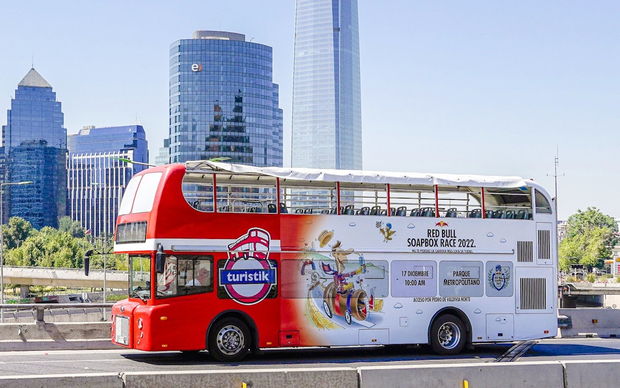 Red double-decker bus on Santiago city tour with skyscrapers in the background.