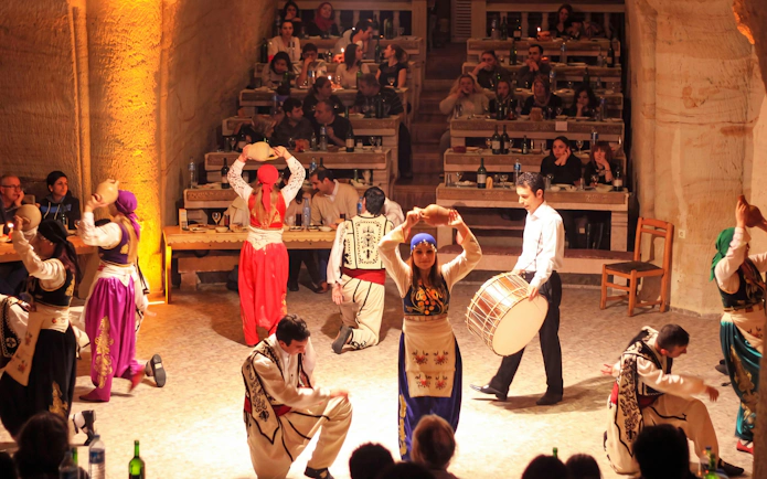 Women in traditional Turkish clothes performing folk dance in a cave restaurant.