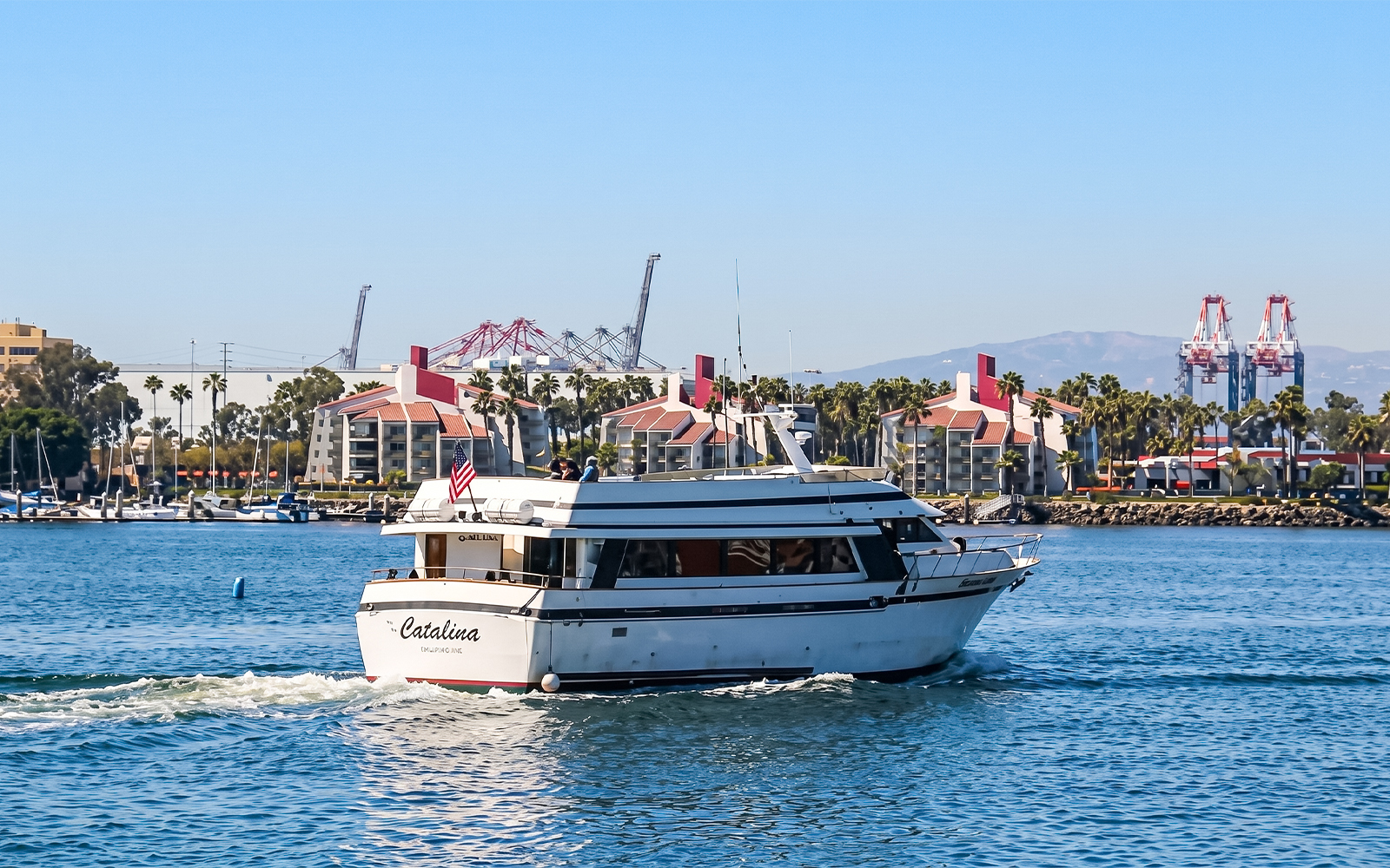 Sightseeing boat cruising in Los Angeles Harbor with cityscape and cranes in the background.