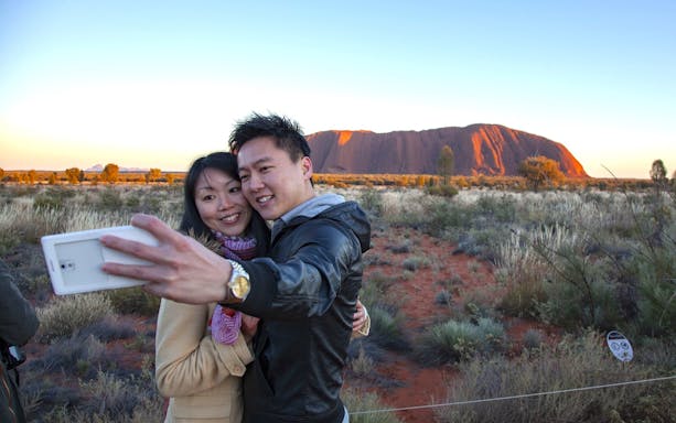 Couple taking a selfie with Uluru in the background during an Outback camping adventure.