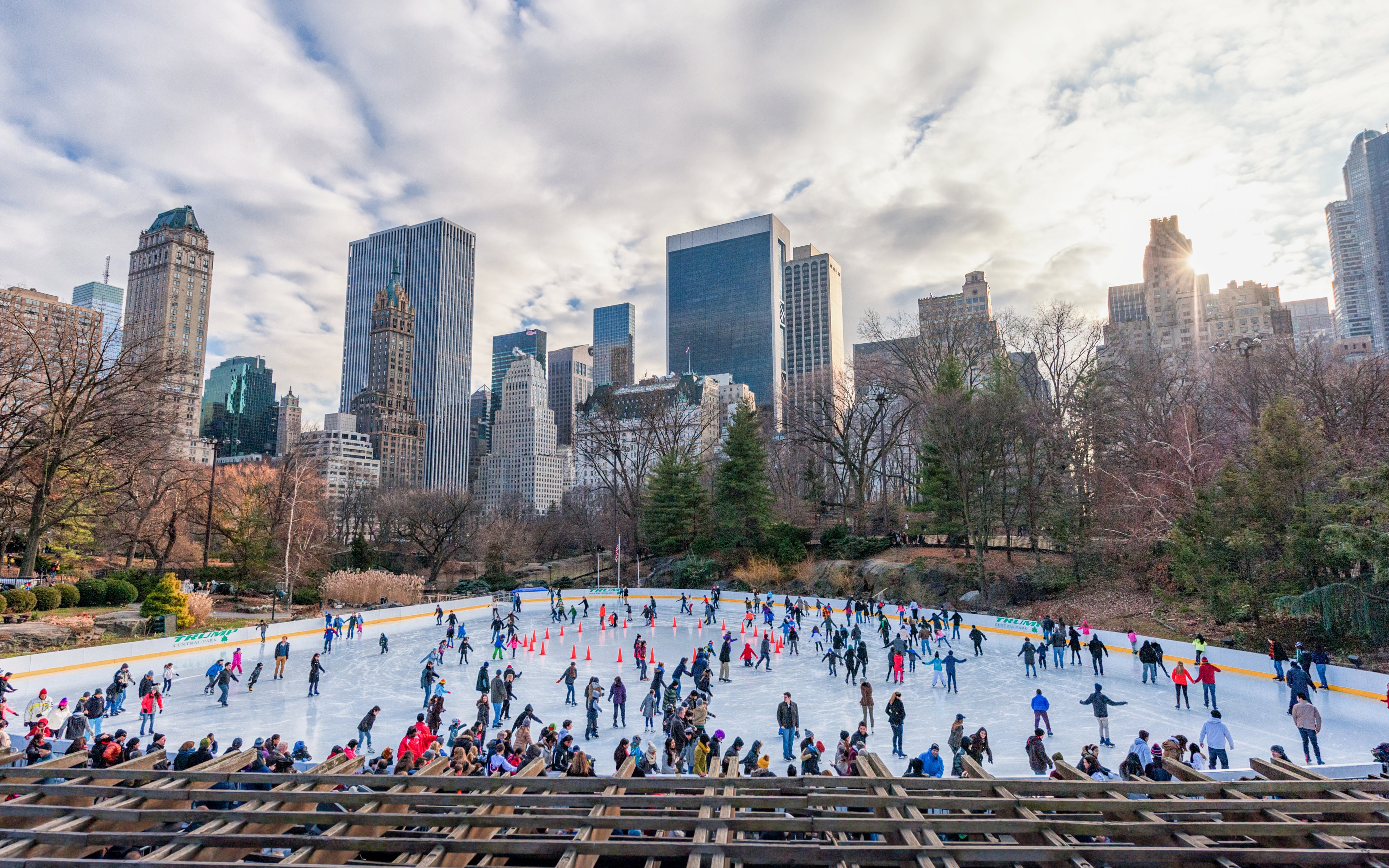 Skaters enjoying Wollman Rink in New York's Central Park with city skyline in the background.