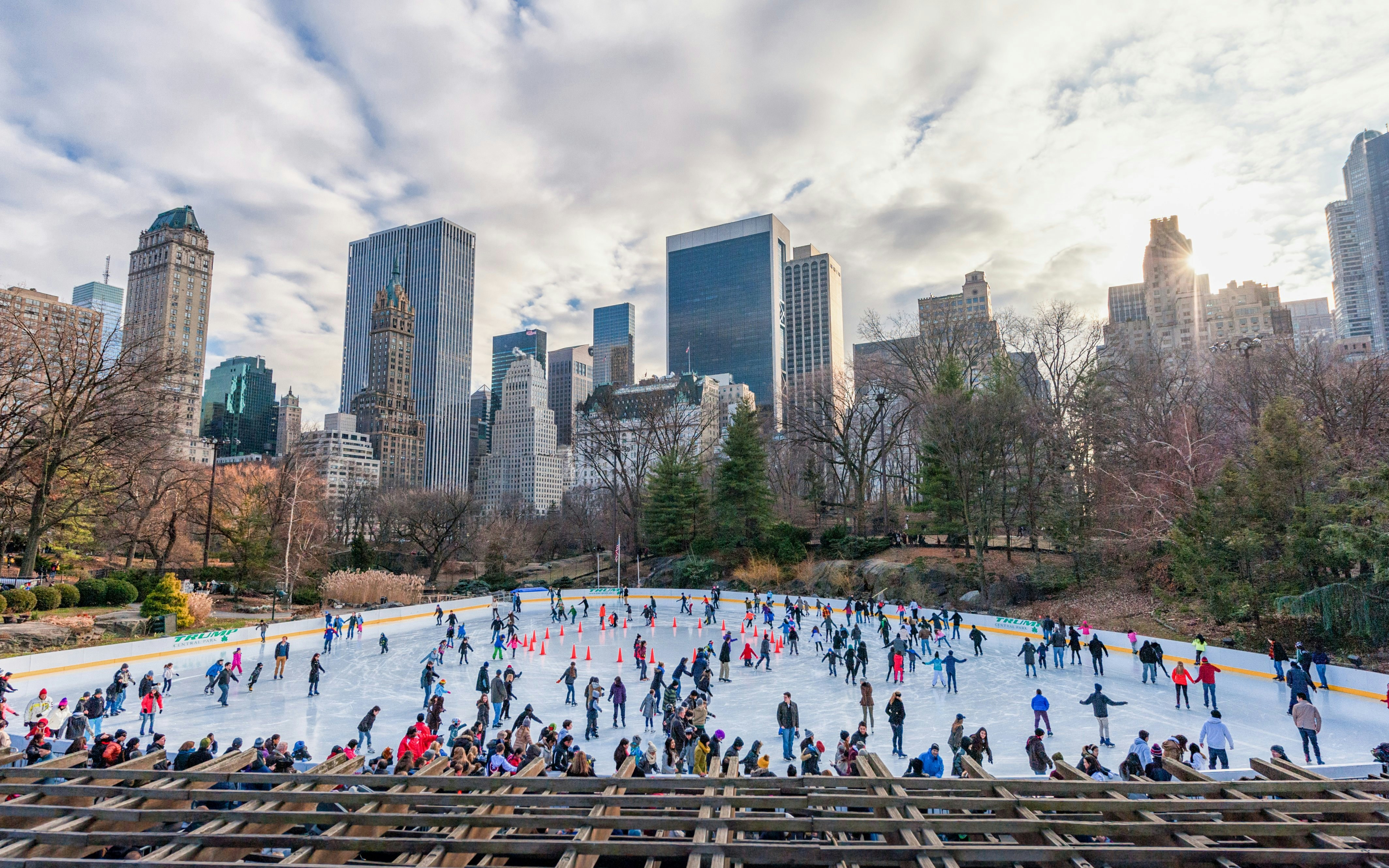 Skaters enjoying Wollman Rink in New York's Central Park with city skyline in the background.