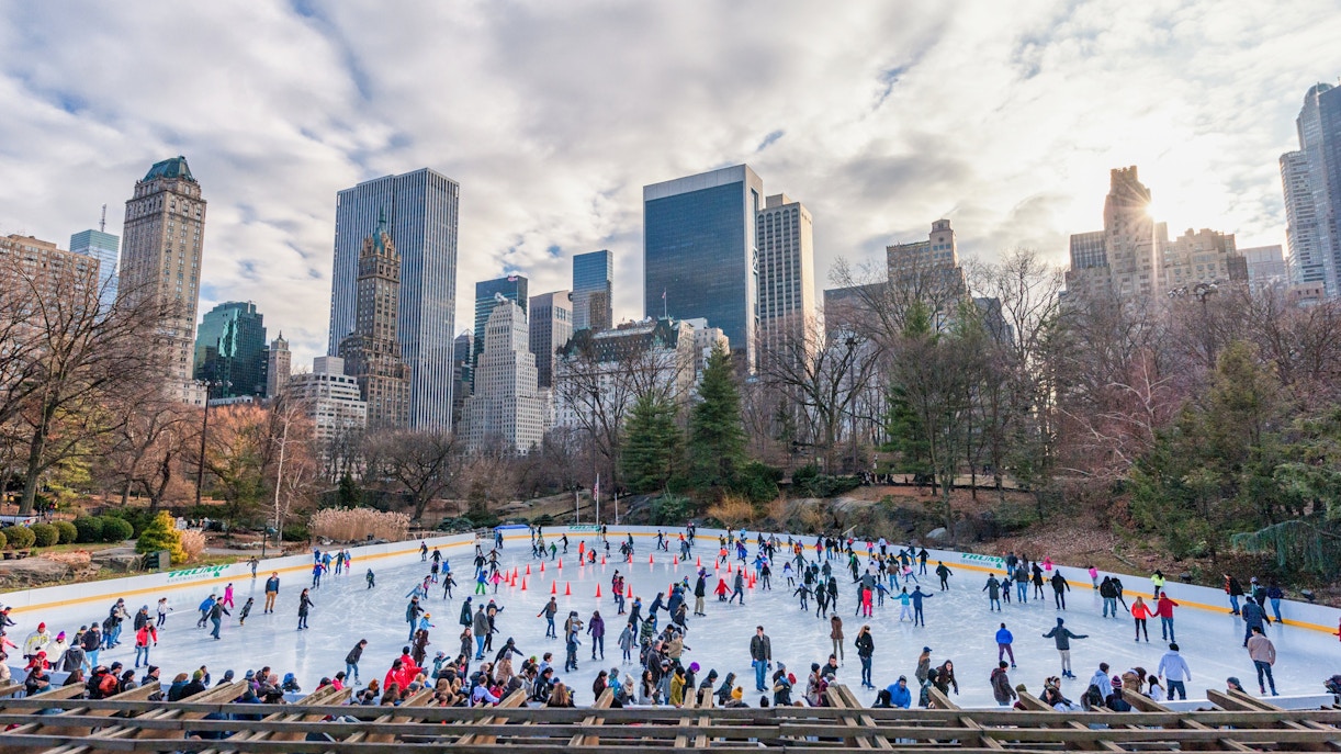 Skaters enjoying Wollman Rink in New York's Central Park with city skyline in the background.