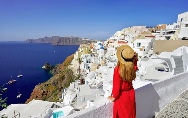 Woman overlooking white buildings and sea in Mykonos, Greece, during a guided day trip from Athens.