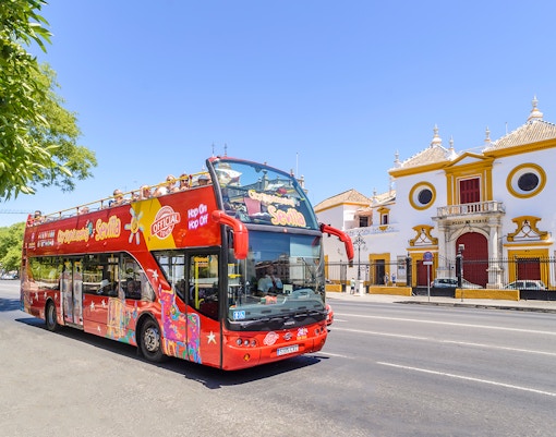 Ônibus hop-on-hop-off Sevilha passando pela Torre del Oro com turistas explorando os pontos turísticos da cidade.