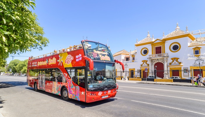 Seville hop-on-hop-off bus passing Torre del Oro with tourists exploring city landmarks.