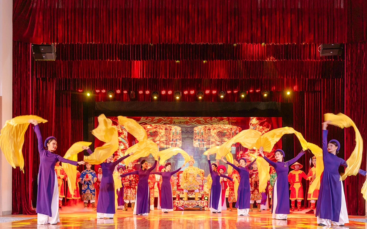 Performers in traditional Ao Dai costumes with yellow scarves at a show in Da Nang.