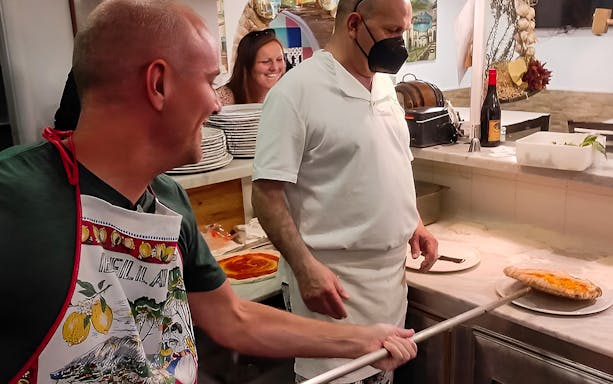 Pizza-making class participants in Naples placing a pizza in the oven.