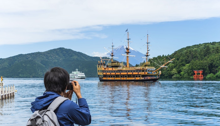 Young traveler photographing pirate ship on Lake Ashi near Hakone Shrine, Japan.