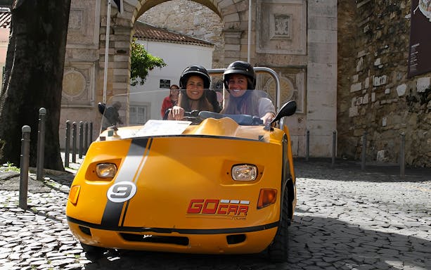 Two people in a yellow GoCar on a cobblestone street in Porto.