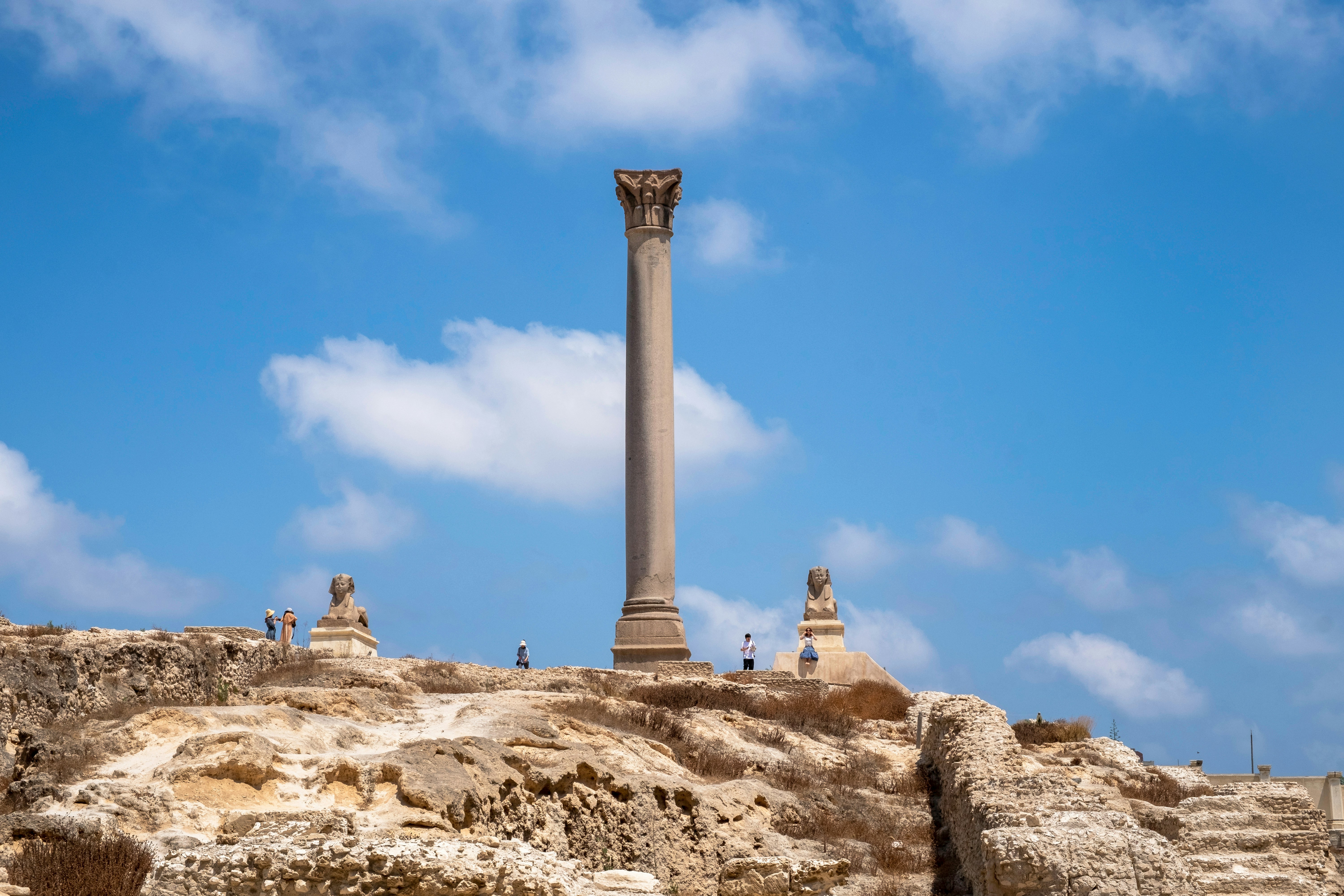 Pompey's Pillar in Alexandria, Egypt, with surrounding ruins and sphinx statues.