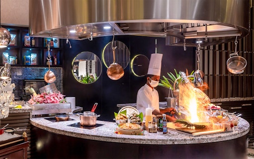 Chef preparing buffet dishes at Mundo Jumeirah Emirates Towers with open flame cooking.