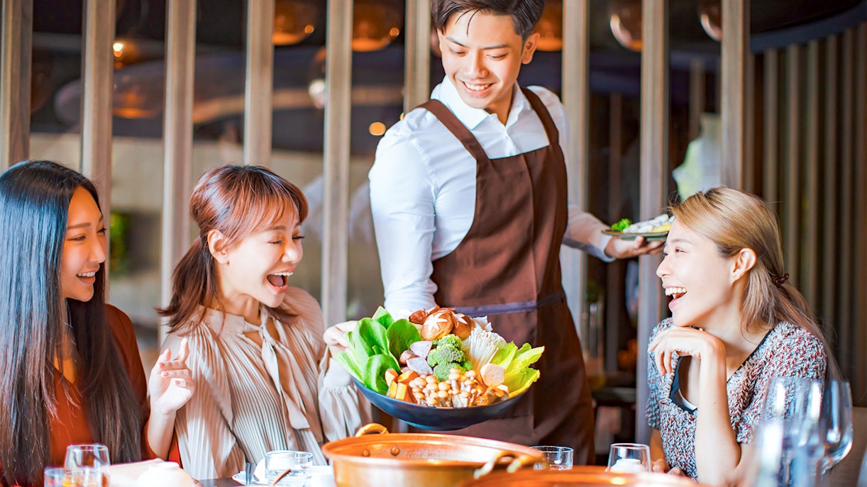 Server presenting a colorful vegetable platter to smiling diners at Atmosphere 360 restaurant.
