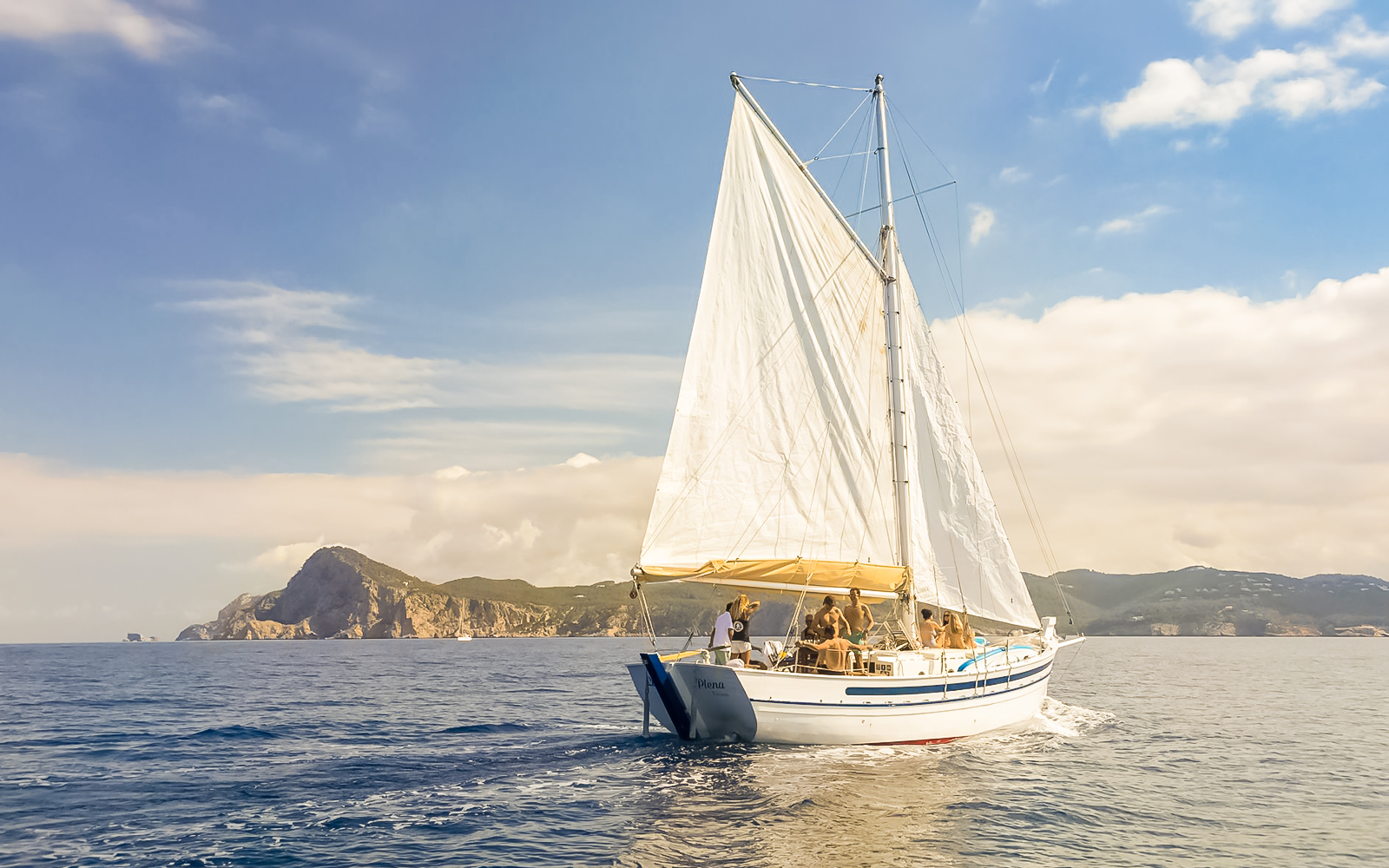 Tourists on a classic sailboat during a private sunset cruise near Ibiza's coastline.