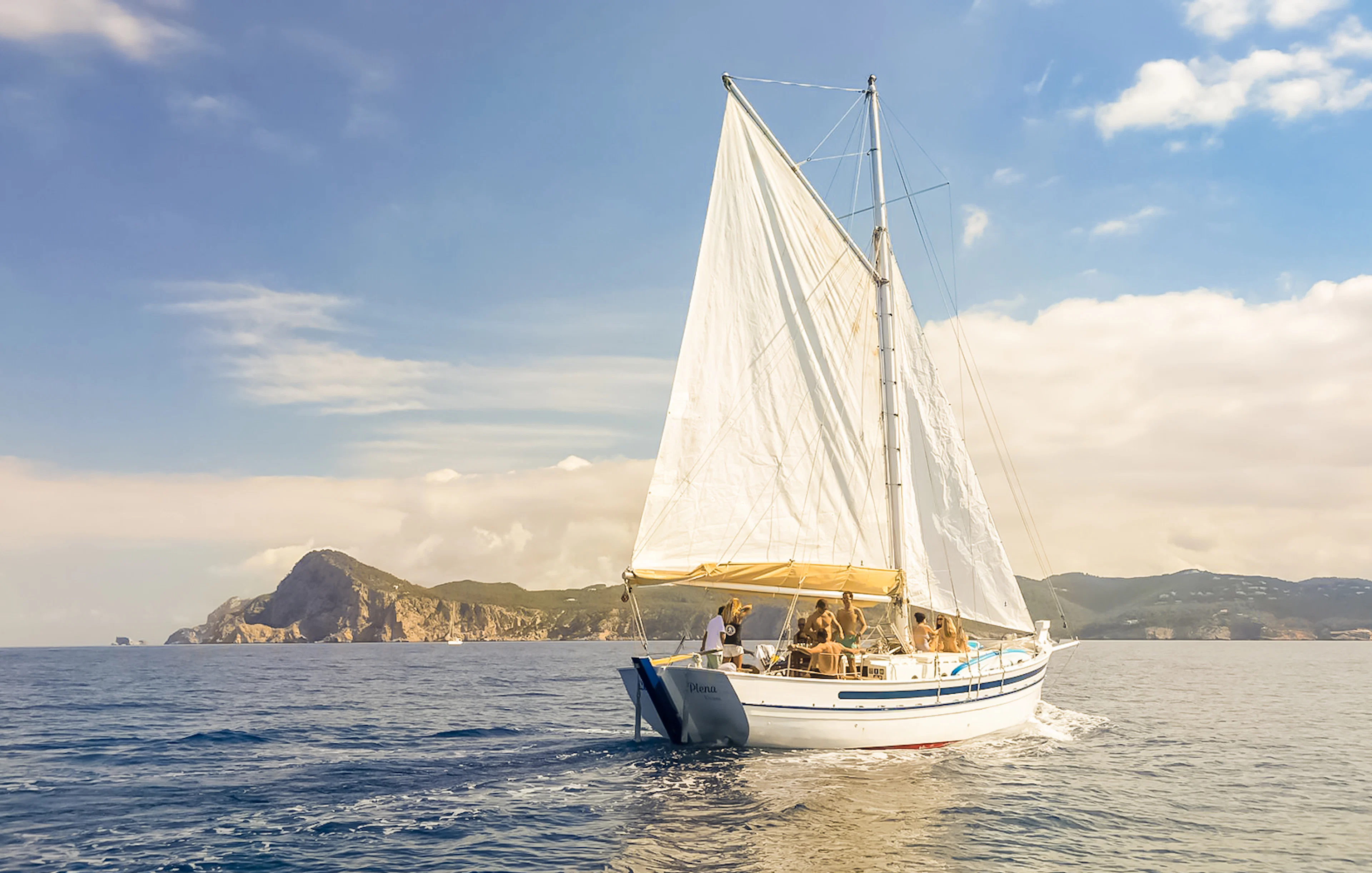 Tourists on a classic sailboat during a private sunset cruise near Ibiza's coastline.